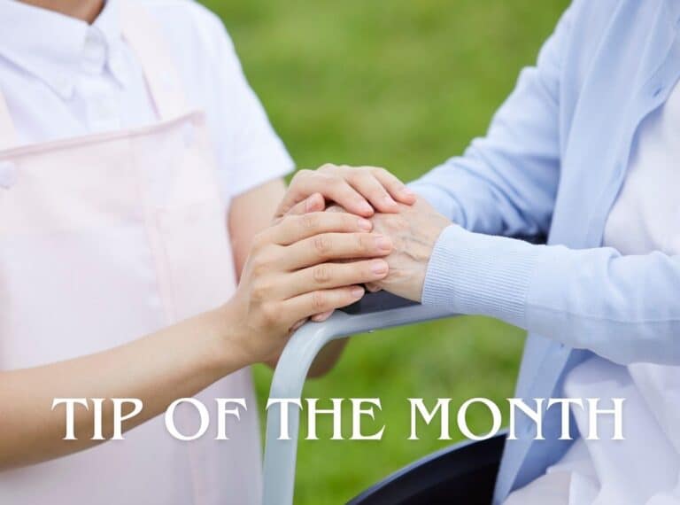 Caregiver and elderly person clasping hands on a walker outdoors, with a 'TIP OF THE MONTH' caption across the bottom.